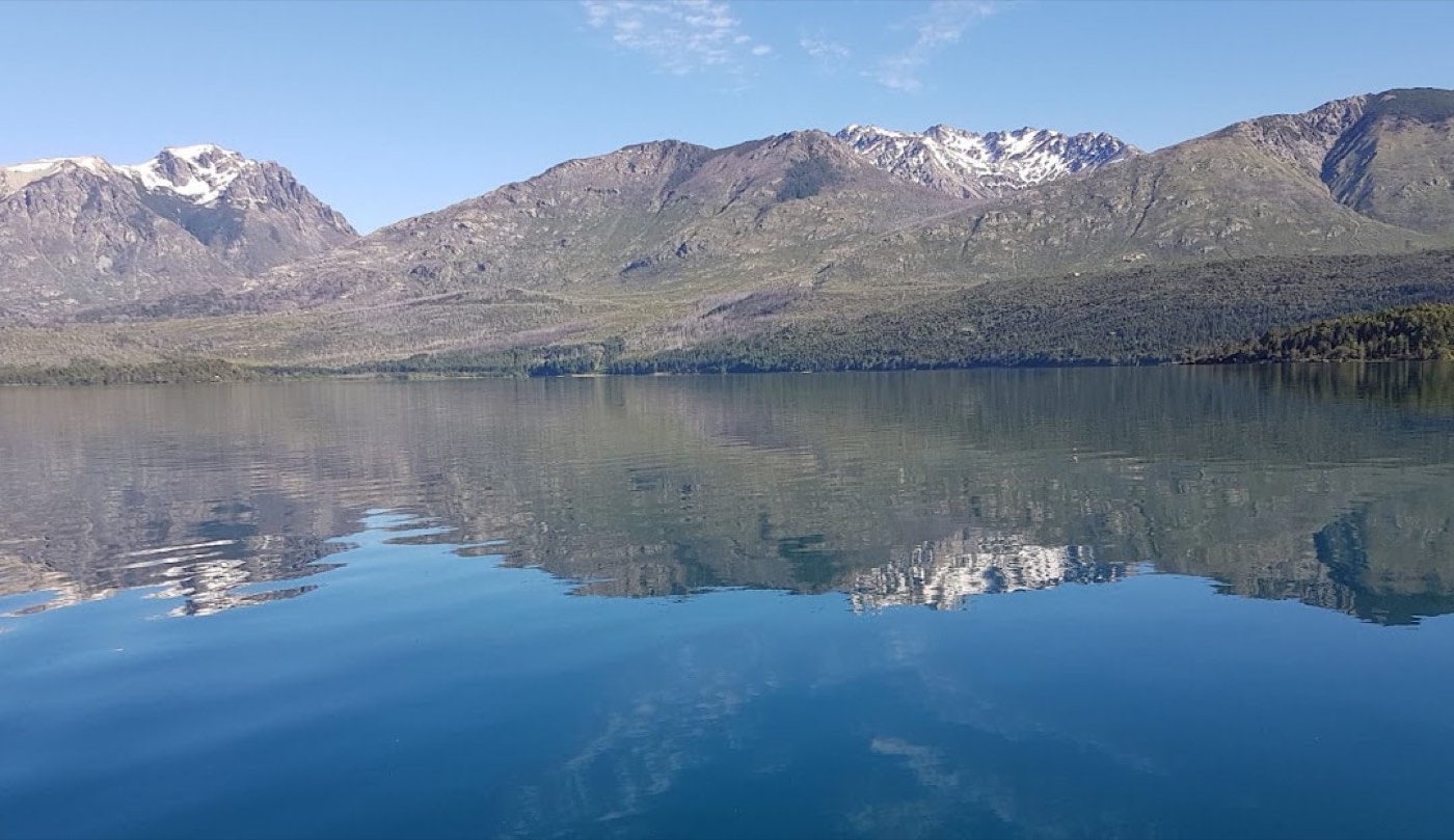 Lago Cholila's glassy water mirroring the surrounding mountains, seen from the lake